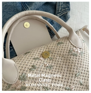 Detail of golden magnetic buckle on straw handbag with floral embroidery and weave texture