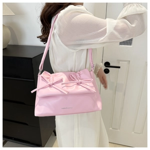 Detail of pink PU leather shoulder bag featuring dual bows and adjustable strap on a model