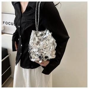 Detail of silver sequin bucket bag with metal chain strap held by a fashion model