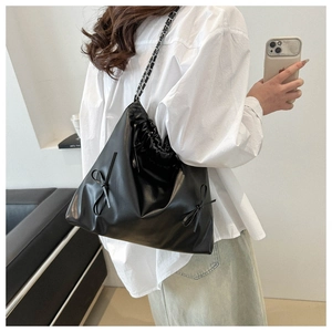 Black tote bag detail featuring drawstring closure, side bow, and chain strap on model
