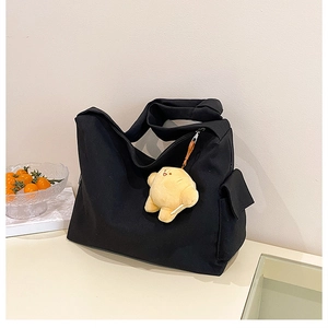 Detail of black canvas tote bag with yellow plush pendant and side cargo pocket