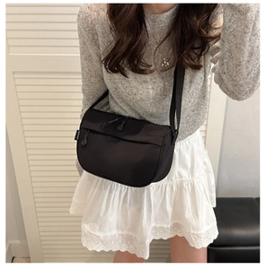 Detail of a black nylon crossbody bag with zipper closure and white textile brand label