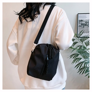 Detail of nylon crossbody bag featuring a wide woven strap and decorative zipper pull