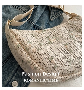 Close-up of woven straw crescent bag featuring delicate floral embroidery and canvas strap
