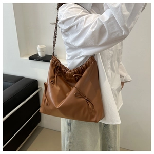 Detail of brown pleated drawstring bucket bag with decorative bows and chain strap