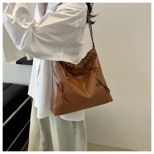 Brown leather shoulder bag with bow details and chain strap shown on a model