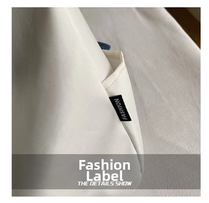 Detailed shot of white tote bag featuring a high-quality stitched FASHION woven label