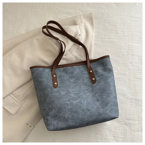Dettaglio della borsa tote grigio-blu con manici marroni e rivetti dorati su giacca beige