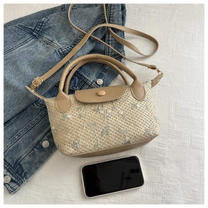 Detailed macro view of floral embroidery on a cream straw woven handbag with leather flap