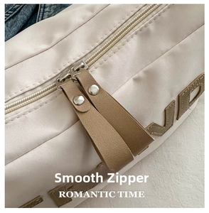 Close-up of smooth dual metal zippers with brown leather pulls on a beige crossbody bag