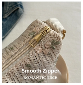Detailed macro view of smooth gold metal zipper and floral embroidery on woven bag