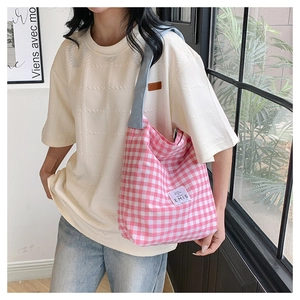 Detail of a pink gingham canvas tote bag with a light blue strap and woven brand label