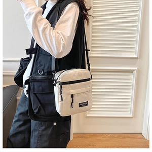 Detail of white canvas crossbody bag with adjustable strap and front zipper compartment