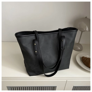 Dettaglio di una grande borsa tote nera su un mobile bianco con oggetti decorativi