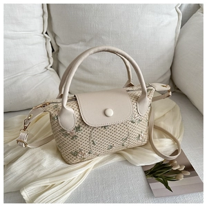 Detail of floral embroidery on a woven straw handbag with a cream leather flap
