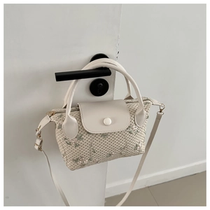 Detail of woven straw handbag with floral embroidery and white PU leather clasp