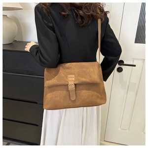 Detail of large brown matte leather tote bag with buckle closure worn by a model