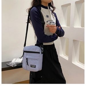 Detail of light purple nylon mini crossbody bag with black zipper pocket and fashion label