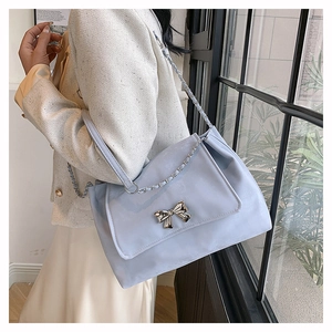 Detail of light blue faux leather shoulder bag featuring a silver metal bow accent