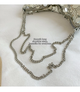 Detailed shot of silver sequin surface and slim metal chain strap on a women's crossbody bag