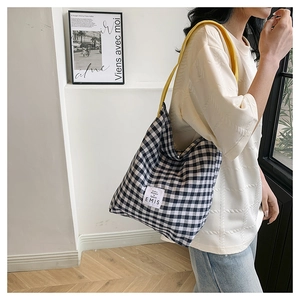 Detail of checkered canvas tote bag with yellow strap and woven label worn by a model