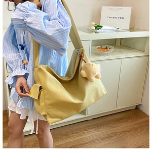 Detail of yellow canvas tote bag with side flap pocket and plush toy charm accessory