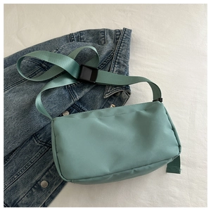 Detail of light green nylon crossbody bag with wide strap and black buckle on denim