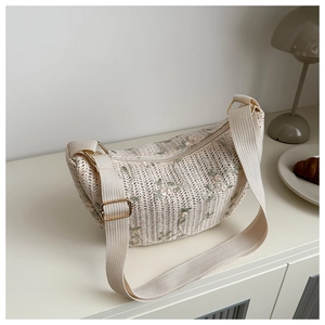 Detailed embroidery of pink flowers on a cream woven lace crescent shoulder bag