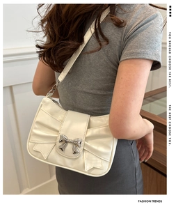 Detail of cream white shoulder bag with large bow design and silver metal clasp