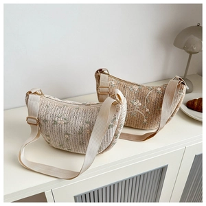 Detail of hand-woven straw crossbody bags with elegant floral embroidery and adjustable straps