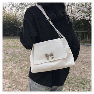White shoulder bag with silver butterfly buckle and chain strap shown on model outdoors