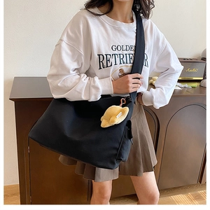 Detail of large black canvas crossbody bag with a cute plush croissant pendant accessory