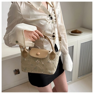 Close-up of a woven mini straw bag with floral embroidery and camel leather flap detail