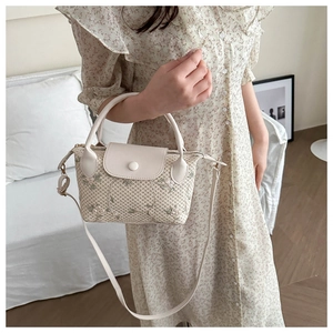 Detail of woven straw handbag with floral embroidery and white synthetic leather strap