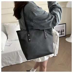 Dettaglio borsa tote nera minimalista con rivetti dorati sulla tracolla in casa