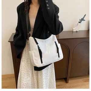 Close-up of white tote bag featuring black zipper details and wide shoulder strap
