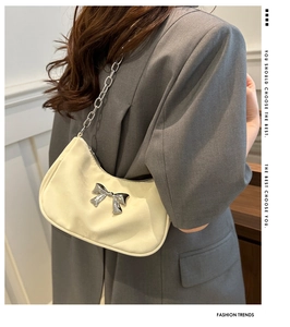 Model wearing a chic beige half-moon underarm bag with a silver metal bow and chain strap