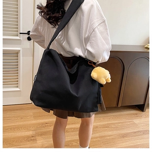 Detail of black canvas crossbody bag with wide strap and yellow chick plush keychain