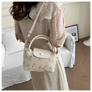 Close-up of woven straw handbag featuring delicate green floral embroidery and leather strap