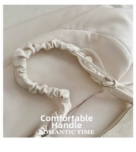 Detail of cream white handbag featuring ruched handle and side drawstring knot detail