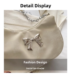 Close-up of creamy white underarm bag with silver bow detail and chain strap texture