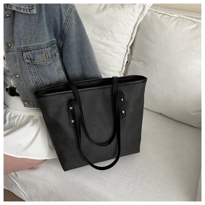 Dettaglio borsa tote nera minimalista con rivetti dorati su un divano bianco