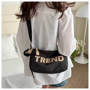 Detail of black crossbody bag with TREND letter patch and fluffy mascot on a model