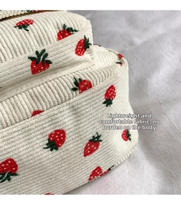 Macro shot of cream corduroy fabric featuring detailed red and green strawberry embroidery