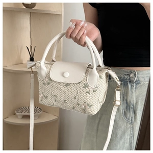 Close-up of white woven handbag with floral embroidery and white leather strap details