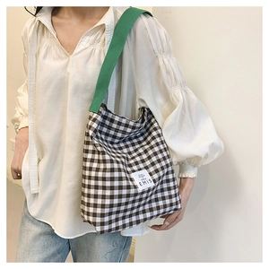 Detail of canvas checkered bucket bag with contrast green strap and brand logo patch