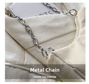 Detail of silver chain strap and zipper on cream-colored bow bag with fabric texture