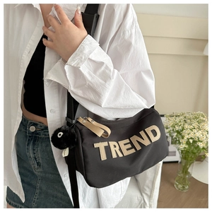 Detail of a black cylinder bag with TREND text, fluffy charm, and beige zipper pull