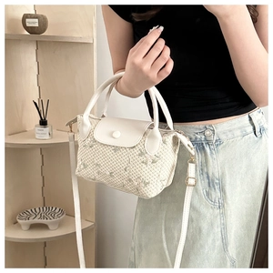 Detail of cream woven handbag with green floral patterns and leather strap in a natural setting
