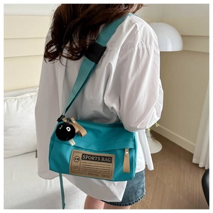 Detail of teal waterproof sports bag with vintage label and black plush sprite pendant